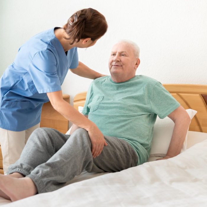 Caregiver assisting elderly man to lie on bed.