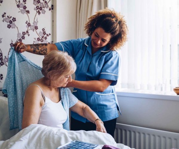 Caregiver dressing up an elderly lady.